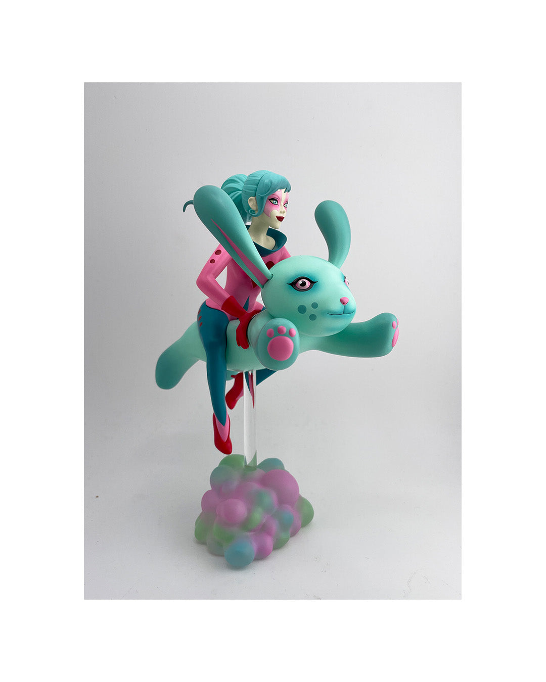 Colorful figurine of a character with teal hair riding a green creature on a white background