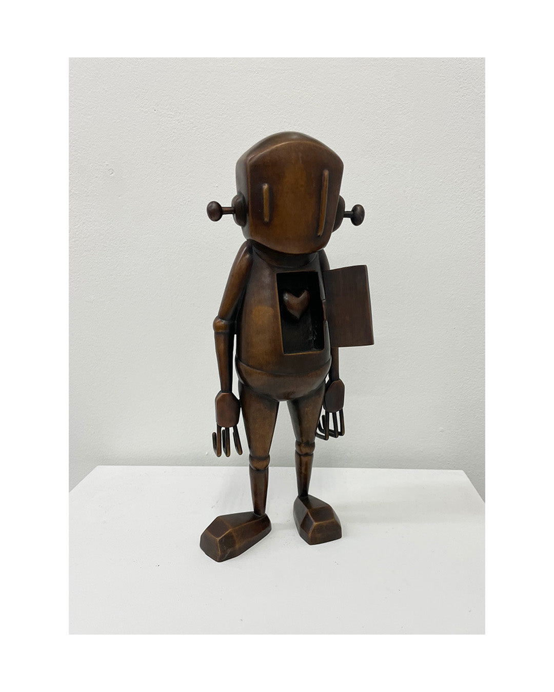 Bronze robot sculpture on a white platform with a light gray background