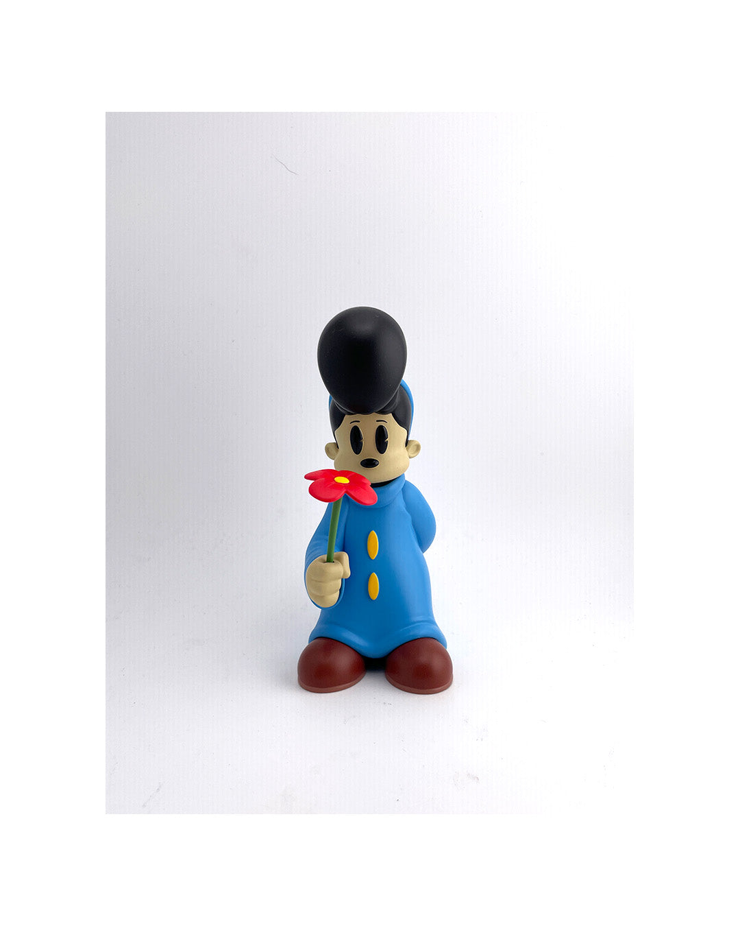 Toy figure of a character in a blue outfit holding a red flower on a white background